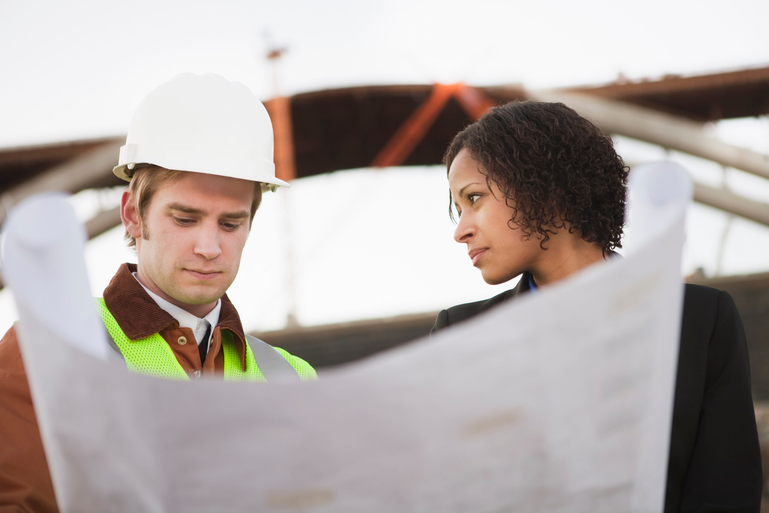 A man in a hard hat and a hi vis and a woman in a suit looking at plans